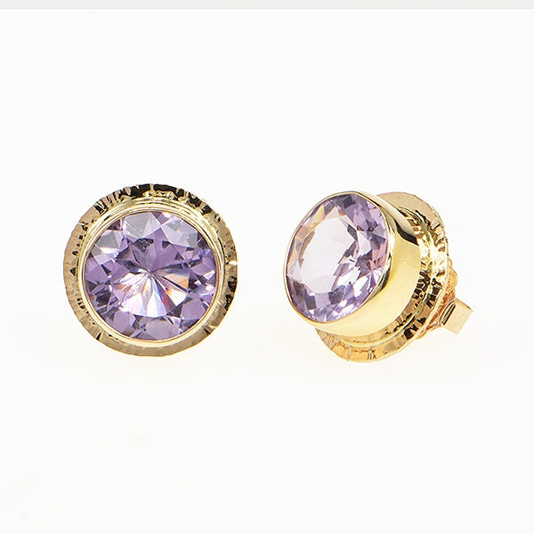 A pair of gold round stud earrings with faceted light purple gemstones, set in a textured gold bezel on a plain white background.